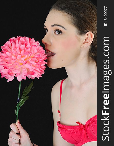 Female model holding a flower licking it in a studio with a black backdrop. Female model holding a flower licking it in a studio with a black backdrop