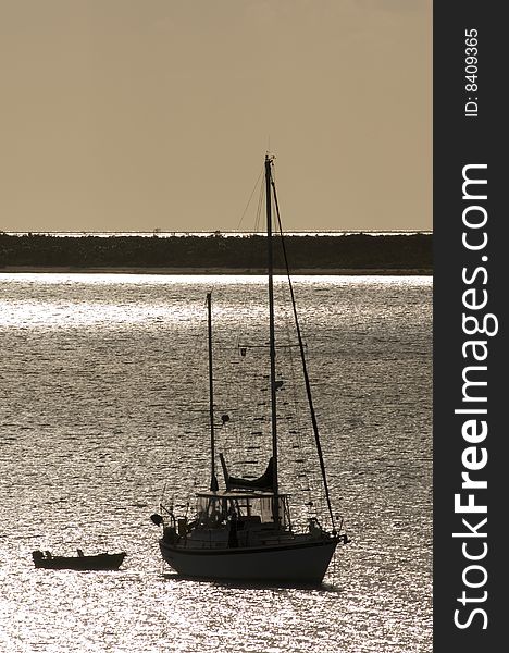 Silhouette of a sailboat and dinghy in a calm harbor on a small island in the Bahamas. Silhouette of a sailboat and dinghy in a calm harbor on a small island in the Bahamas