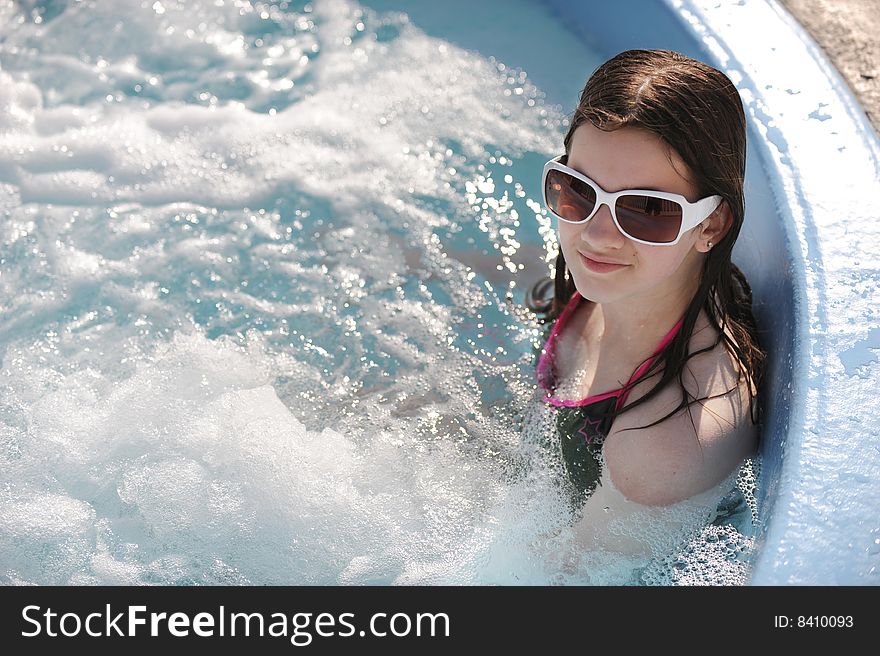 A preteen girl soaking in an outdoor hot tub on a sunny day. A preteen girl soaking in an outdoor hot tub on a sunny day.