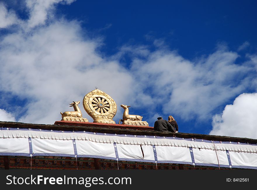 Tourists Resting beside the Golden Buddhism Emblem at the rooftop of a monastery