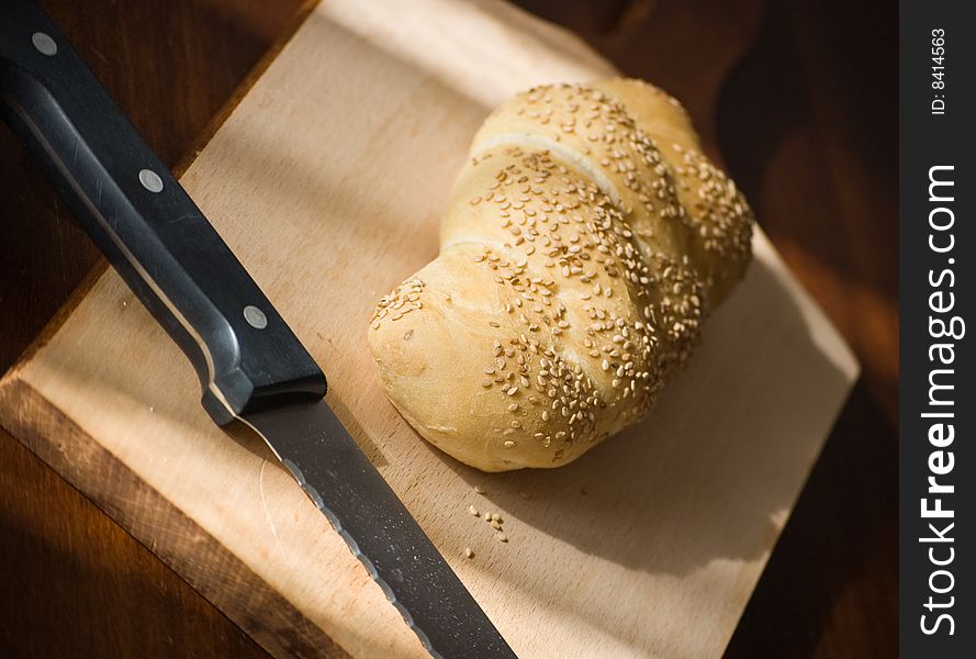 A bread loaf on a wooden table, with a knife ready. A bread loaf on a wooden table, with a knife ready
