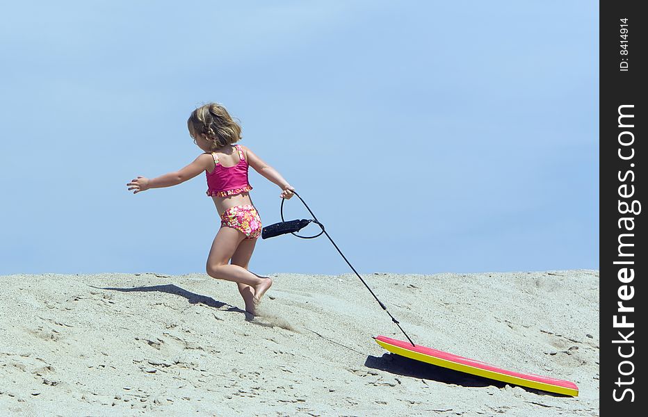 Little girl running up a sand dune while pulling a boogy board behind her. Little girl running up a sand dune while pulling a boogy board behind her