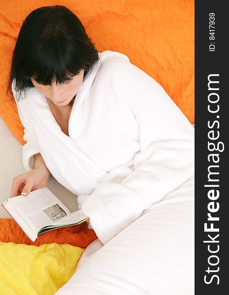 Brunette woman at home in bed reading a book. Brunette woman at home in bed reading a book