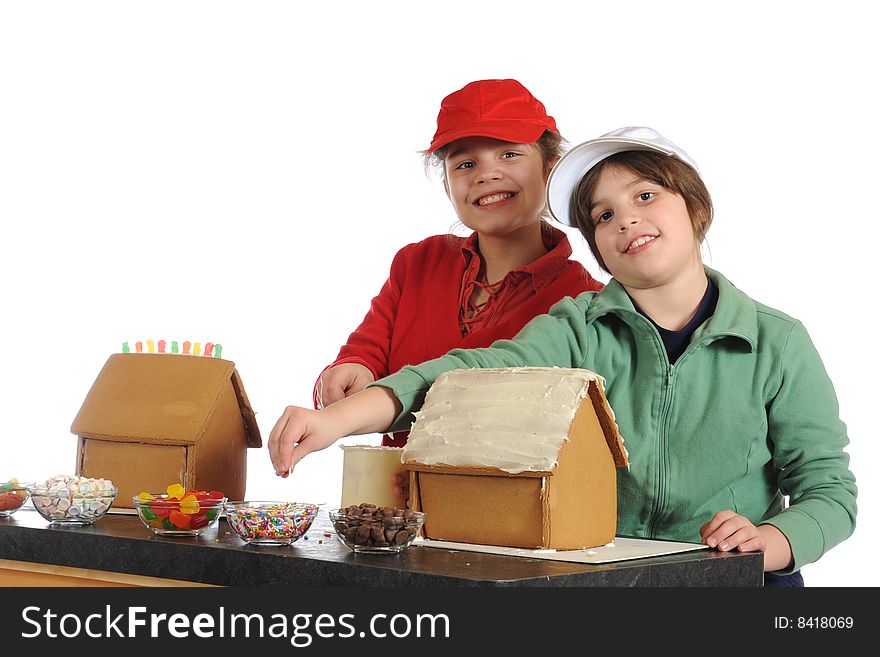 Two girls delighted to be making gingerbread houses for the holidays.  Isolated on white.