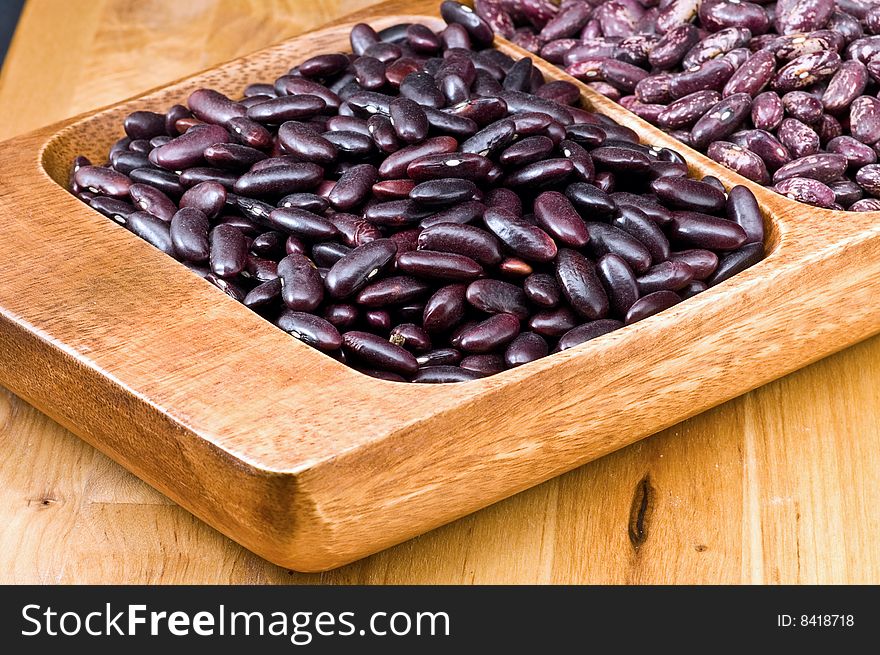 A couple of dark red and spotted kidney beans in wooden dish