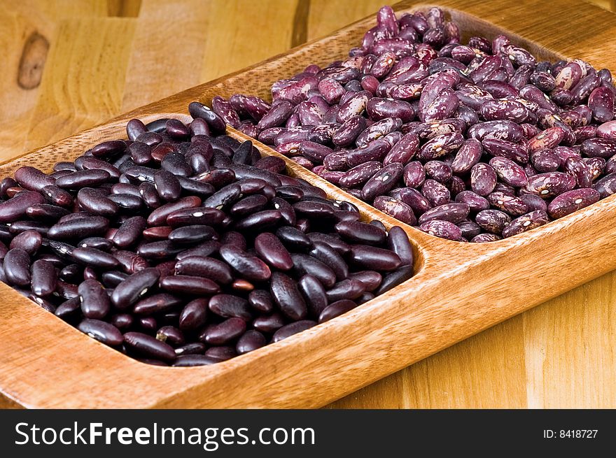 A couple of dark red and spotted kidney beans in wooden dish
