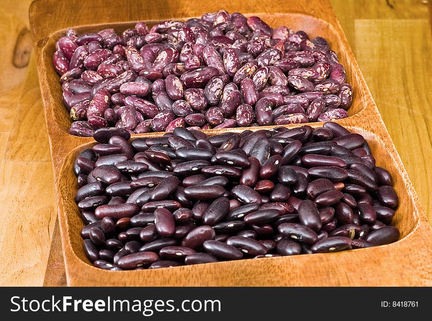 A couple of dark red and spotted kidney beans in wooden dish