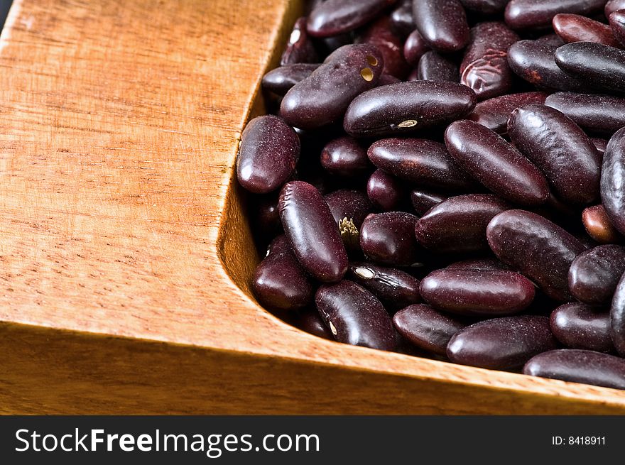 A couple of dark red and spotted kidney beans in wooden dish