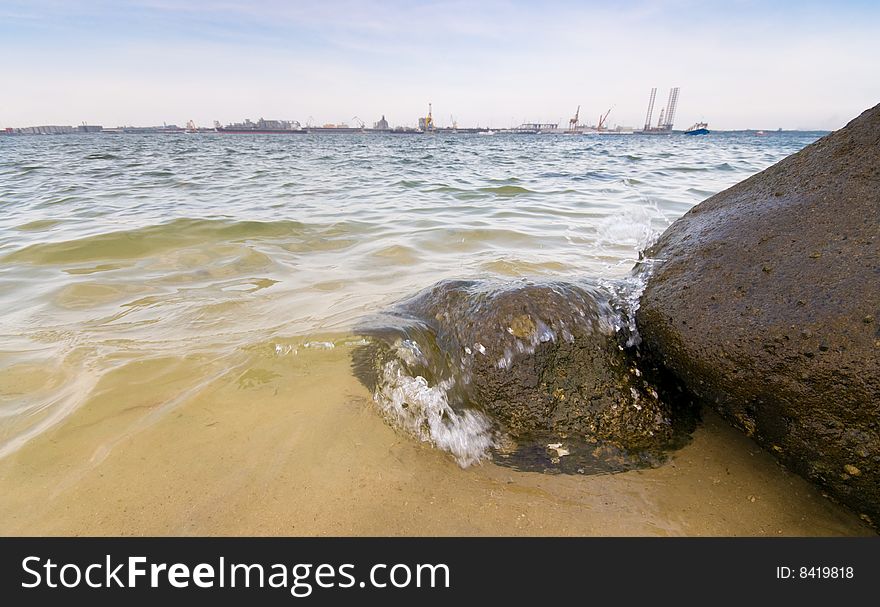 View across a straits of an industrial and port complex from a rocky beach