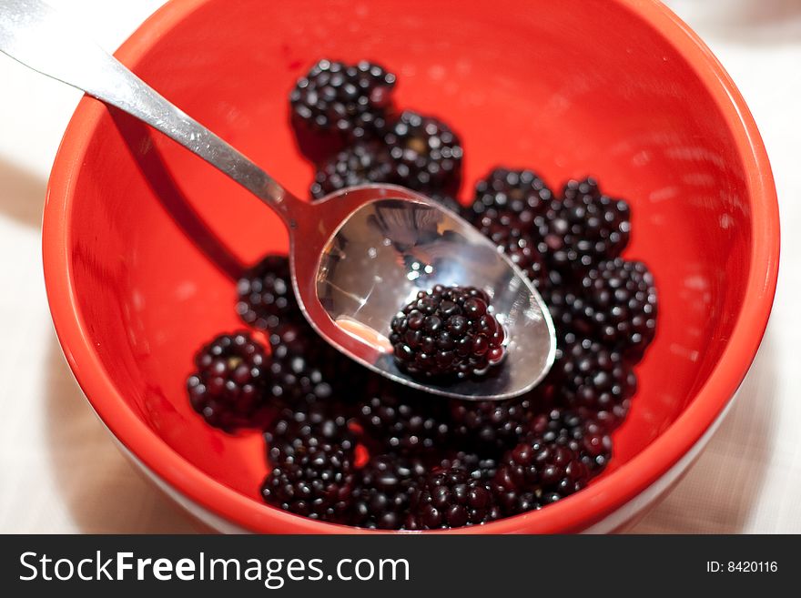 Blackberries in a red bowl with silver spoon