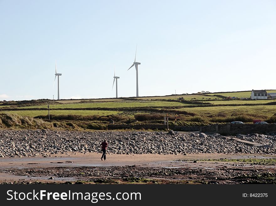 Man running on beale beach co kerry ireland on a cold winters morning with turbines in the background. Man running on beale beach co kerry ireland on a cold winters morning with turbines in the background