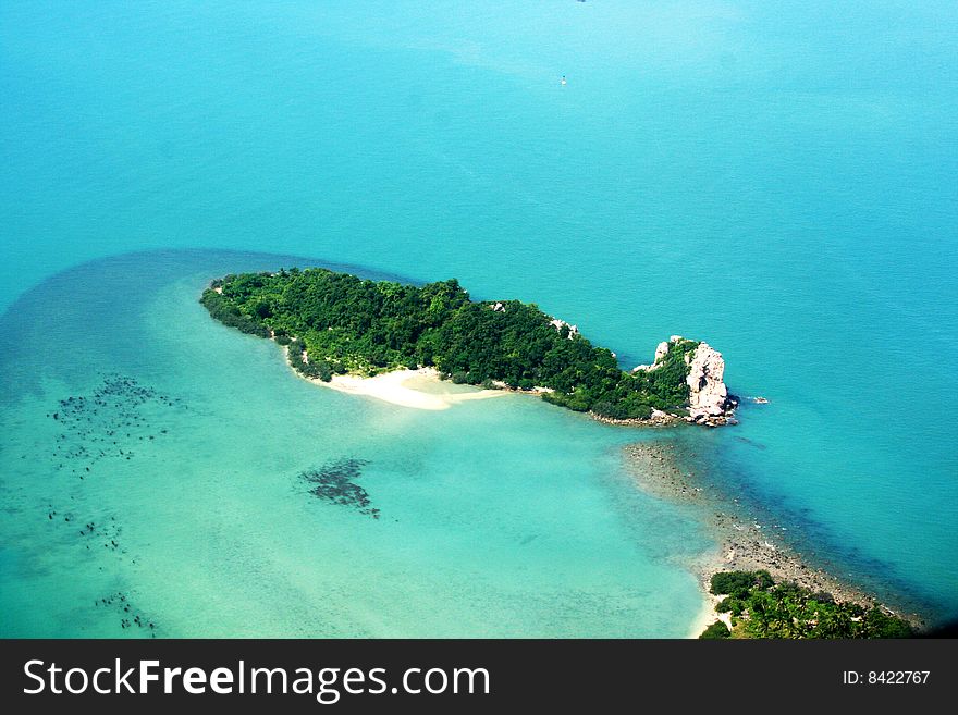 Small green island with white sand in blue water of ocean
