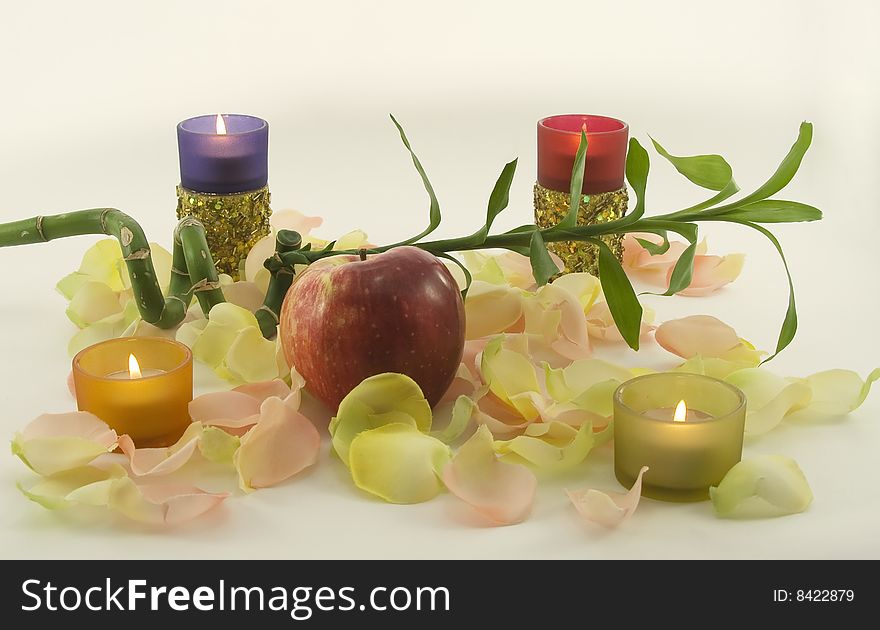 Bamboo and big red fresh apple with aromatic rose leave in rays of color candles. Bamboo and big red fresh apple with aromatic rose leave in rays of color candles