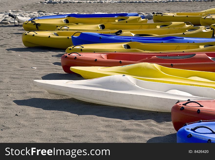 Bright white, yellow, red and blue canoes lie on sandy beach. Bright white, yellow, red and blue canoes lie on sandy beach