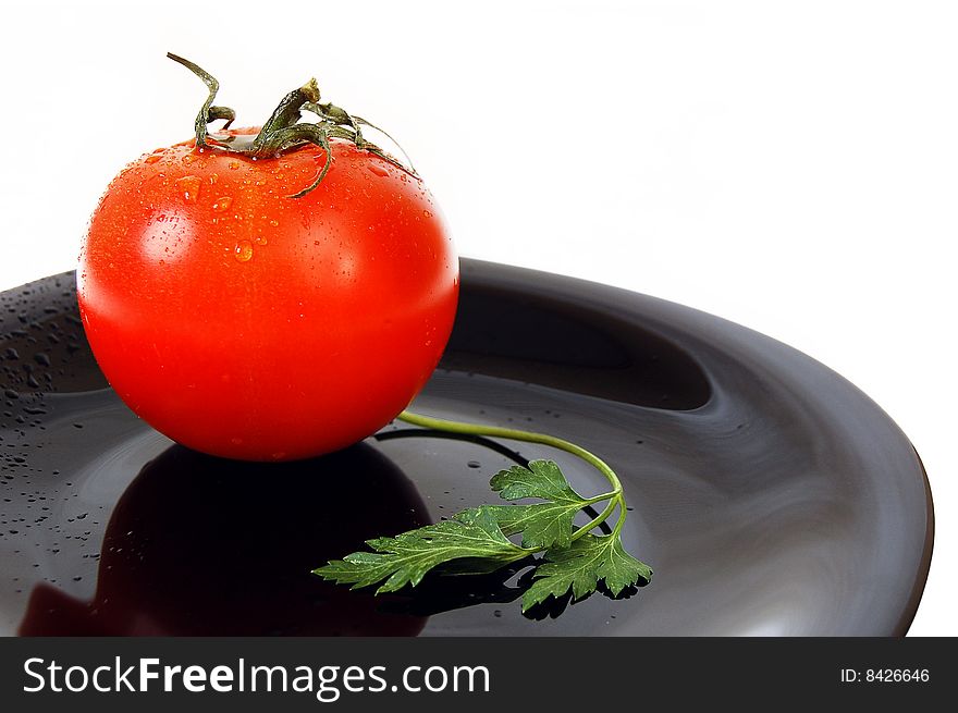 Wet red tomato with fresh parsley on the black plate. White background.