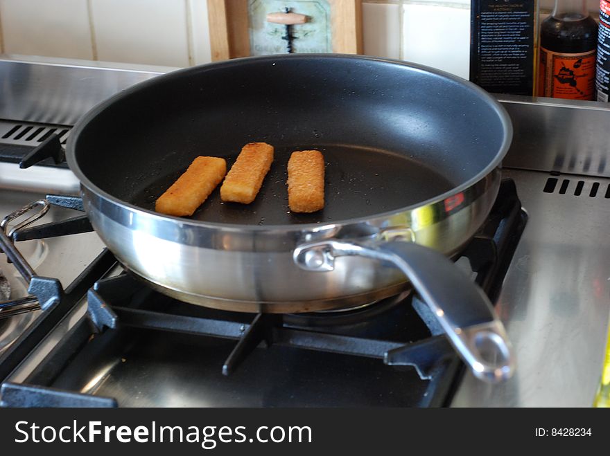 Three fish fingers cooking in a pan, on top of a gas cooker. Three fish fingers cooking in a pan, on top of a gas cooker