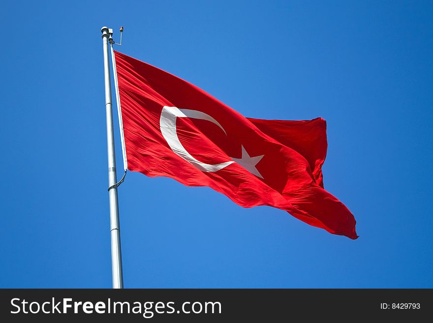 Turkish flag on flagpole against blue sky