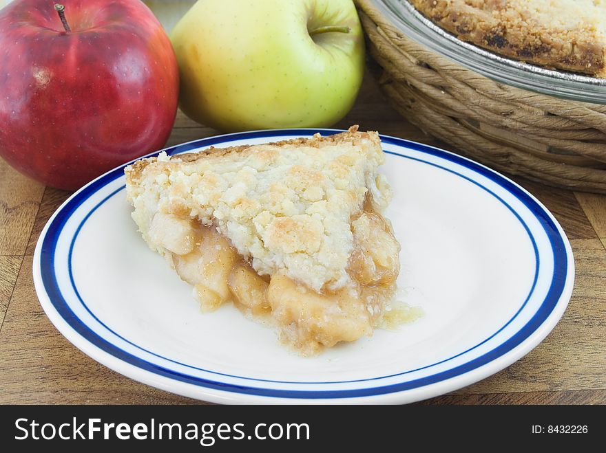 Piece of dutch apple pie on plate with apples and pie behind. Piece of dutch apple pie on plate with apples and pie behind