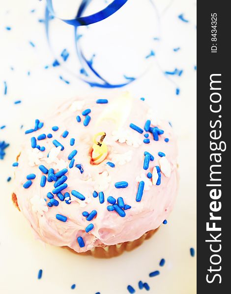 A pink frosted cupcake with blue sprinkles and a candle taken from above it. A pink frosted cupcake with blue sprinkles and a candle taken from above it.