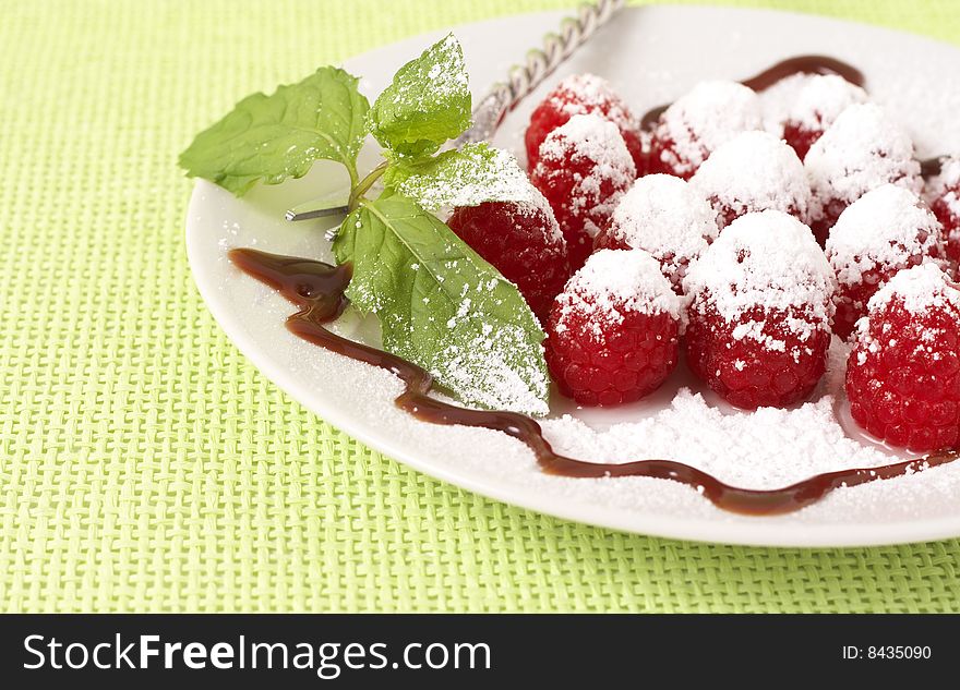 Fresh raspberry dessert served on a white plate, garnished with mint, chocolate sauce and icing sugar. Fresh raspberry dessert served on a white plate, garnished with mint, chocolate sauce and icing sugar