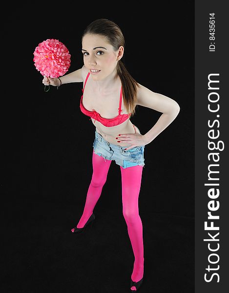 Female model standing in fashionable clothing holding a bright pink flower on a black background. Female model standing in fashionable clothing holding a bright pink flower on a black background