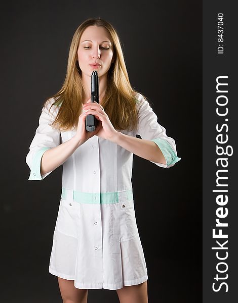 Girl in a doctor's dress with gun on a dark background. Girl in a doctor's dress with gun on a dark background