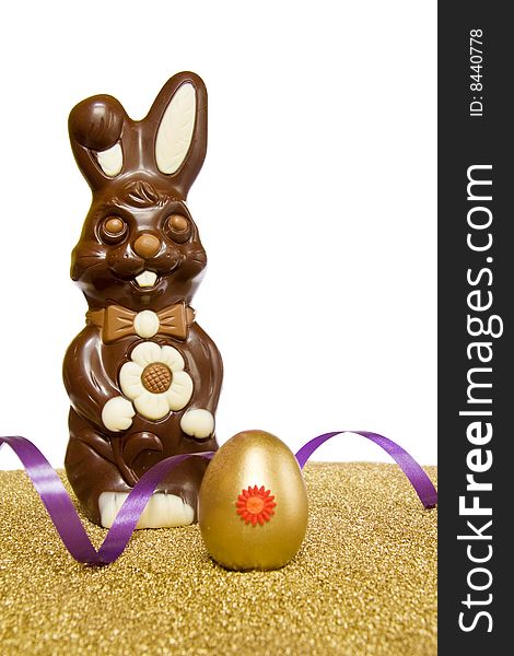 Easter spring celebration with chocolate bunny, golden egg and purple ribbon. Isolated on white with clipping path included. Easter spring celebration with chocolate bunny, golden egg and purple ribbon. Isolated on white with clipping path included.