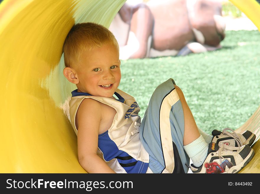 Color image of a young boy in a yellow tunnel at the park. Color image of a young boy in a yellow tunnel at the park.