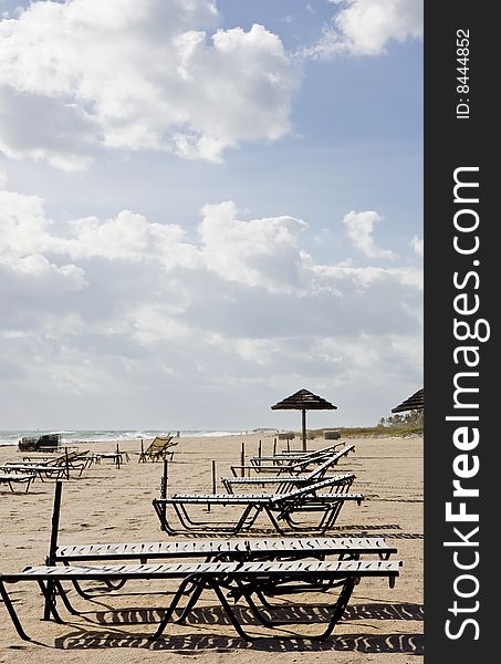 Chaise Lounges and umbrellas on an empty beach under cloudy skies. Chaise Lounges and umbrellas on an empty beach under cloudy skies