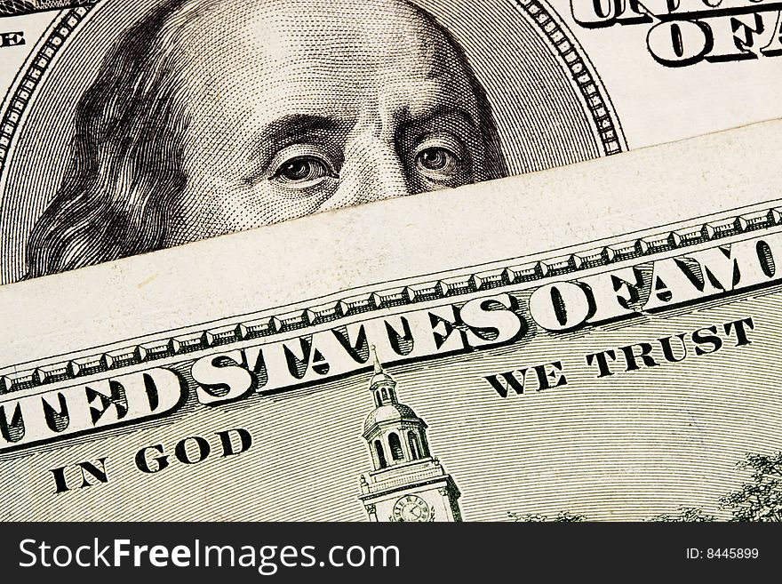 A closeup of a US 100 dollar bill with Benjamin Franklin's face covered with In God We Trust.