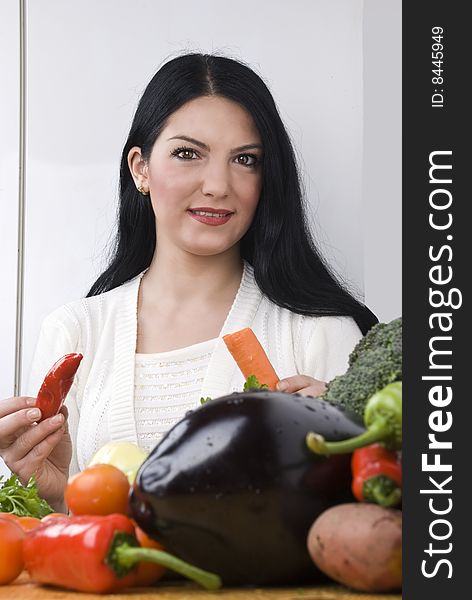 Young brunette woman in kitchen with fresh vegetables holding a red pepper and a carrot.Check out also Healthy food. Young brunette woman in kitchen with fresh vegetables holding a red pepper and a carrot.Check out also Healthy food