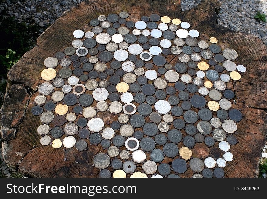 All kind of coins, old and new, fixed in a stump of a tree with rusty nails, making a table. All kind of coins, old and new, fixed in a stump of a tree with rusty nails, making a table.