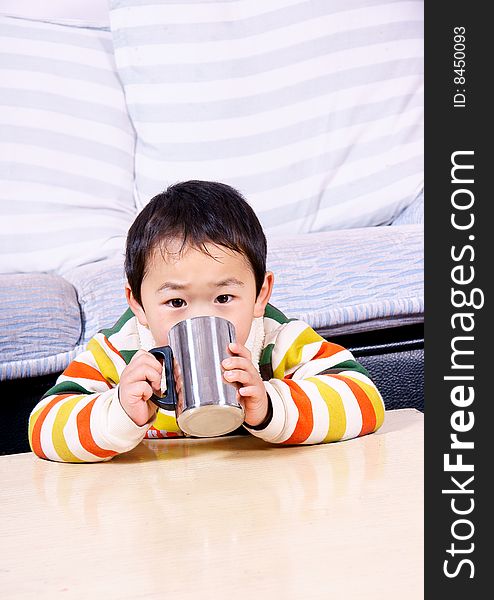 A picture of a little chinese boy drinking water under sofa at home