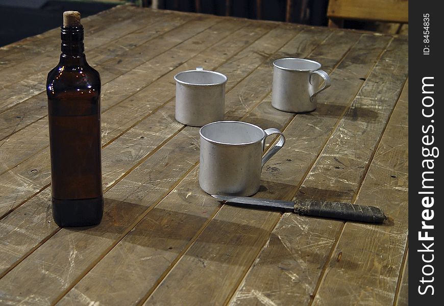 Three mugs, knife and bottle of whisky on a wooden table. Three mugs, knife and bottle of whisky on a wooden table