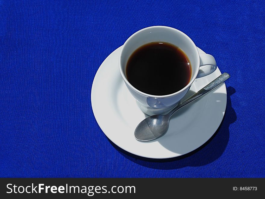 Black coffee in white cup with plate and spoon on blue background