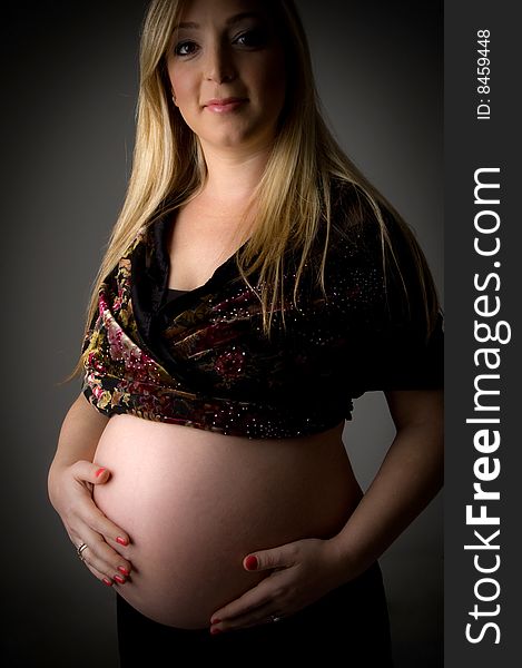 Side view of smiling pregnant female holding her tummy on an isolated background