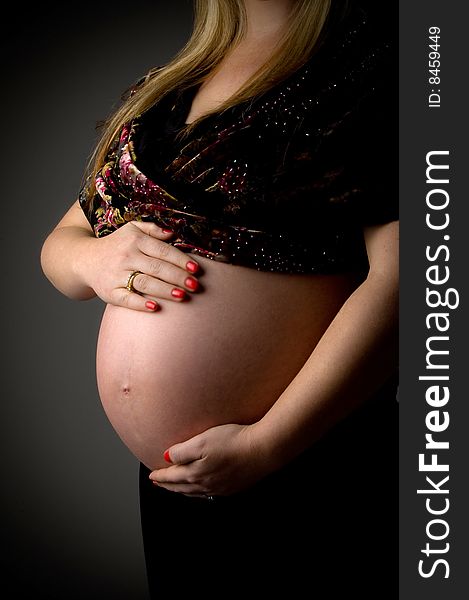 Side view of pregnant female holding her tummy against white background