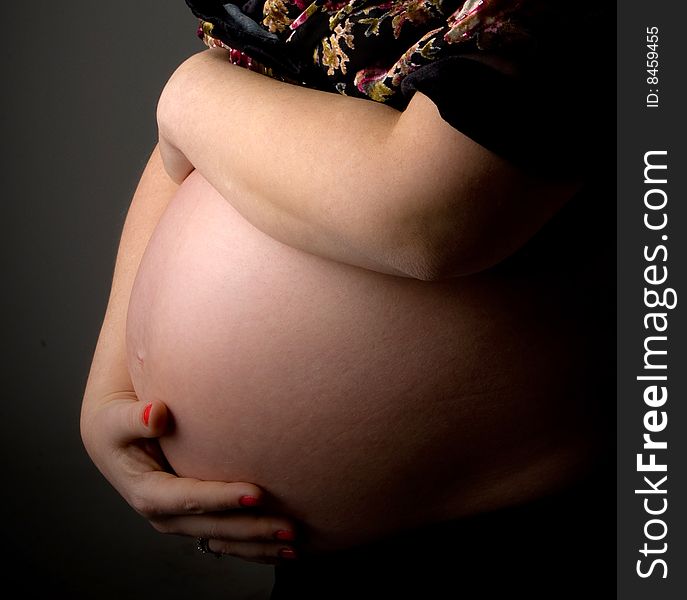 Side view of pregnant woman's tummy with her hands against white background