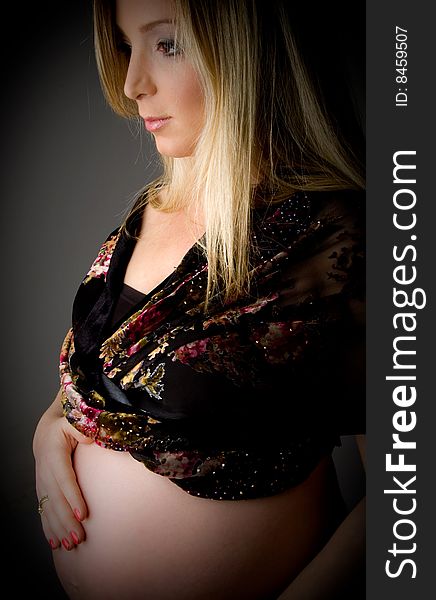 Side view of pregnant female touching her tummy against white background