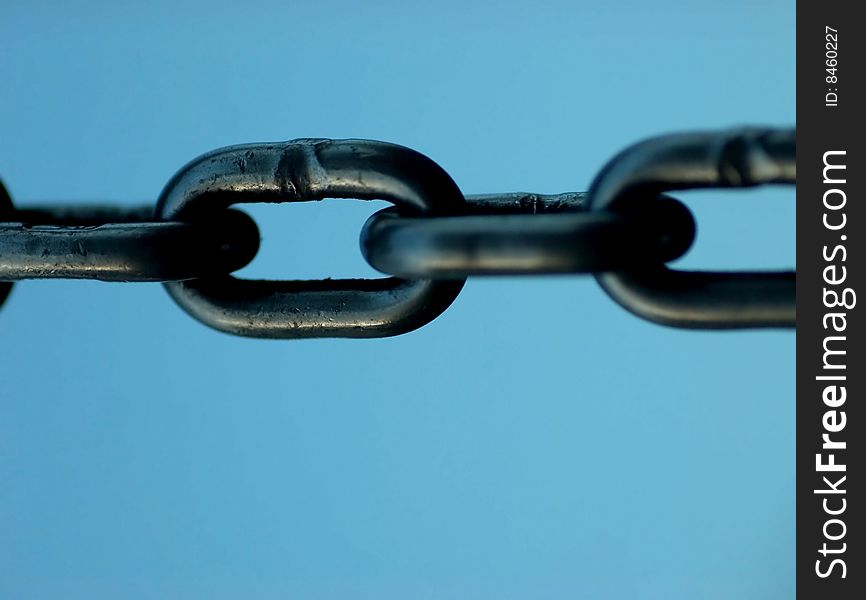 Links of a chain against a blue sky, shallow dof, focus is on the center link