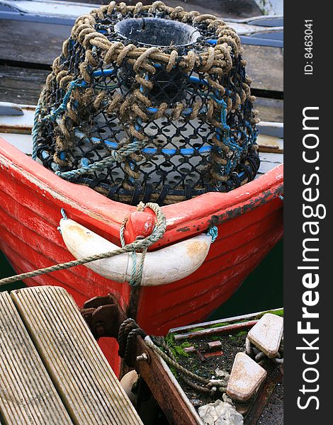 A Lobster and Crab pot at the front of a small red fishing boat located at Salcombe Bay, Devon England UK. A Lobster and Crab pot at the front of a small red fishing boat located at Salcombe Bay, Devon England UK.