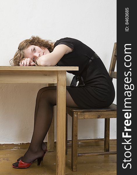 Upset girl in black dress and red shoes put her head down table. Woman`s problem.