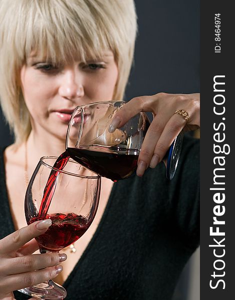 The blonde pours from a glass in a glass red wine. The blonde pours from a glass in a glass red wine.