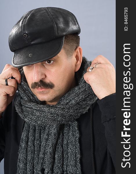 The moustached man in a black shirt and a cap is wrapped up by a scarf. The moustached man in a black shirt and a cap is wrapped up by a scarf.