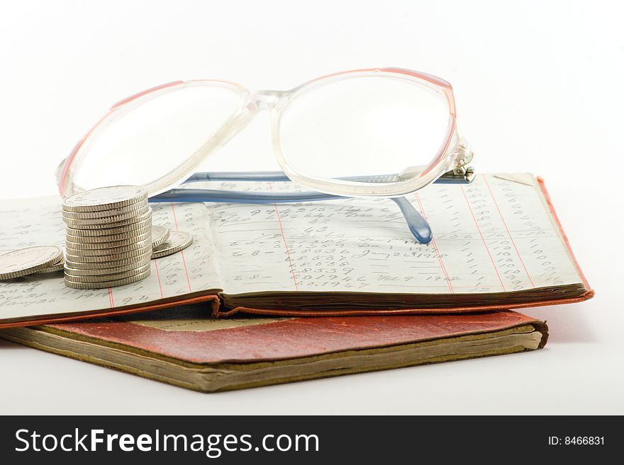 Two financial ledgers with a pair of spectacles and a pile of coins on a white background. Two financial ledgers with a pair of spectacles and a pile of coins on a white background