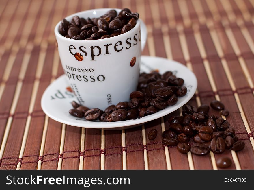 Coffee cup and saucer filled with coffee beans on bamboo place mat