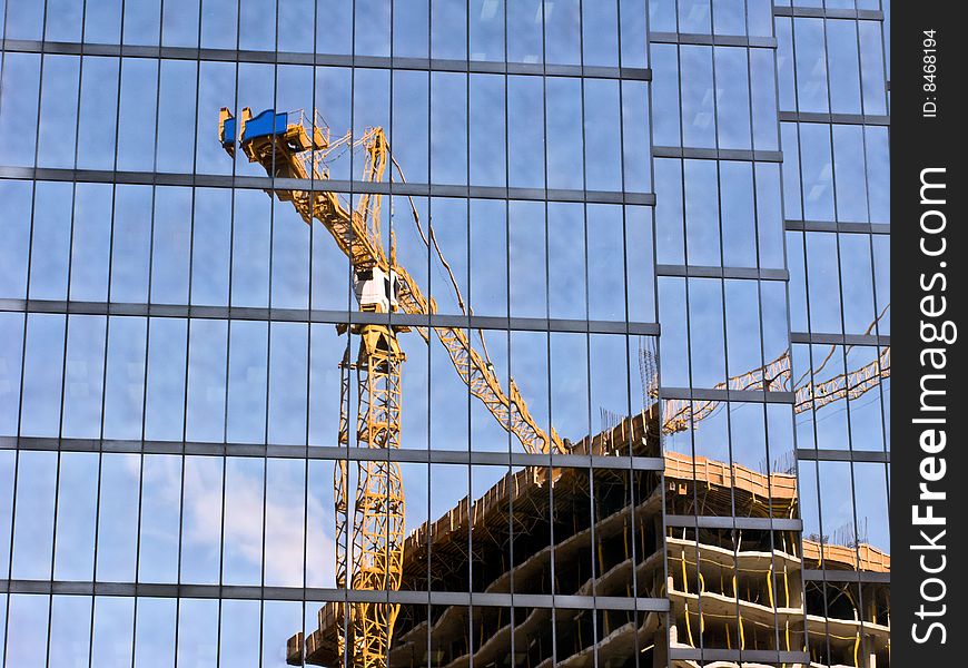 A modern tinted glass skyscraper reflects construction on a neighboring skyscraper. A modern tinted glass skyscraper reflects construction on a neighboring skyscraper.