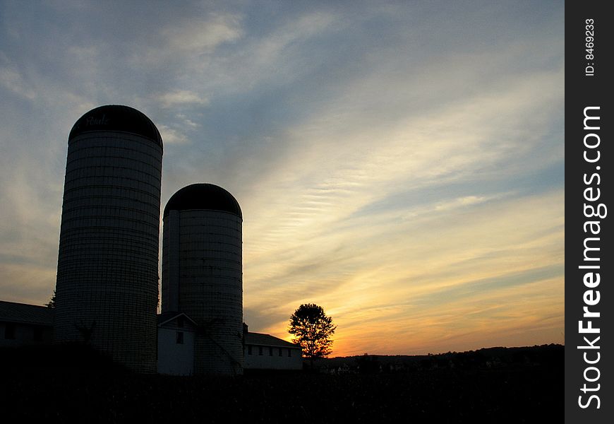 Two old Silos reaching for the evening sky, while the sun is setting in the the horizon. Two old Silos reaching for the evening sky, while the sun is setting in the the horizon.