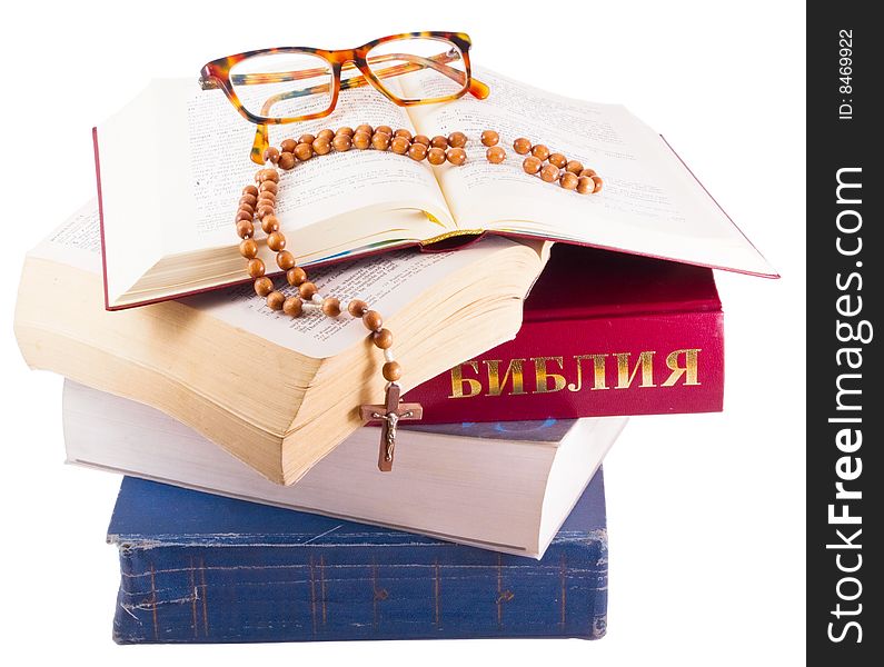 Open Holy Bible lying on stack of old books with glasses, cross and beads isolated. Open Holy Bible lying on stack of old books with glasses, cross and beads isolated