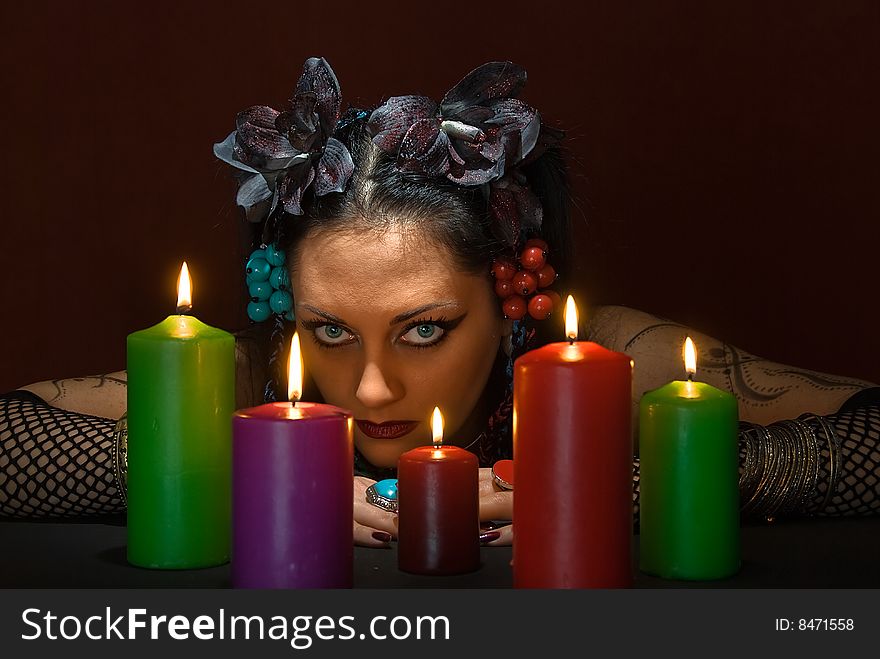 Young beautiful soothsayer with five candles on dark red background. Young beautiful soothsayer with five candles on dark red background